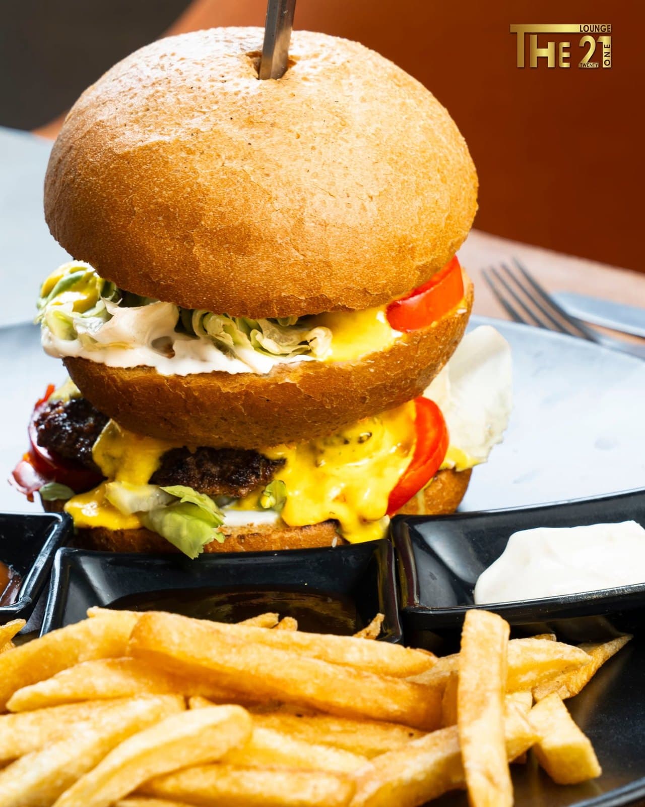 Burger garni, accompagné de frites et de sauces sur une assiette noire