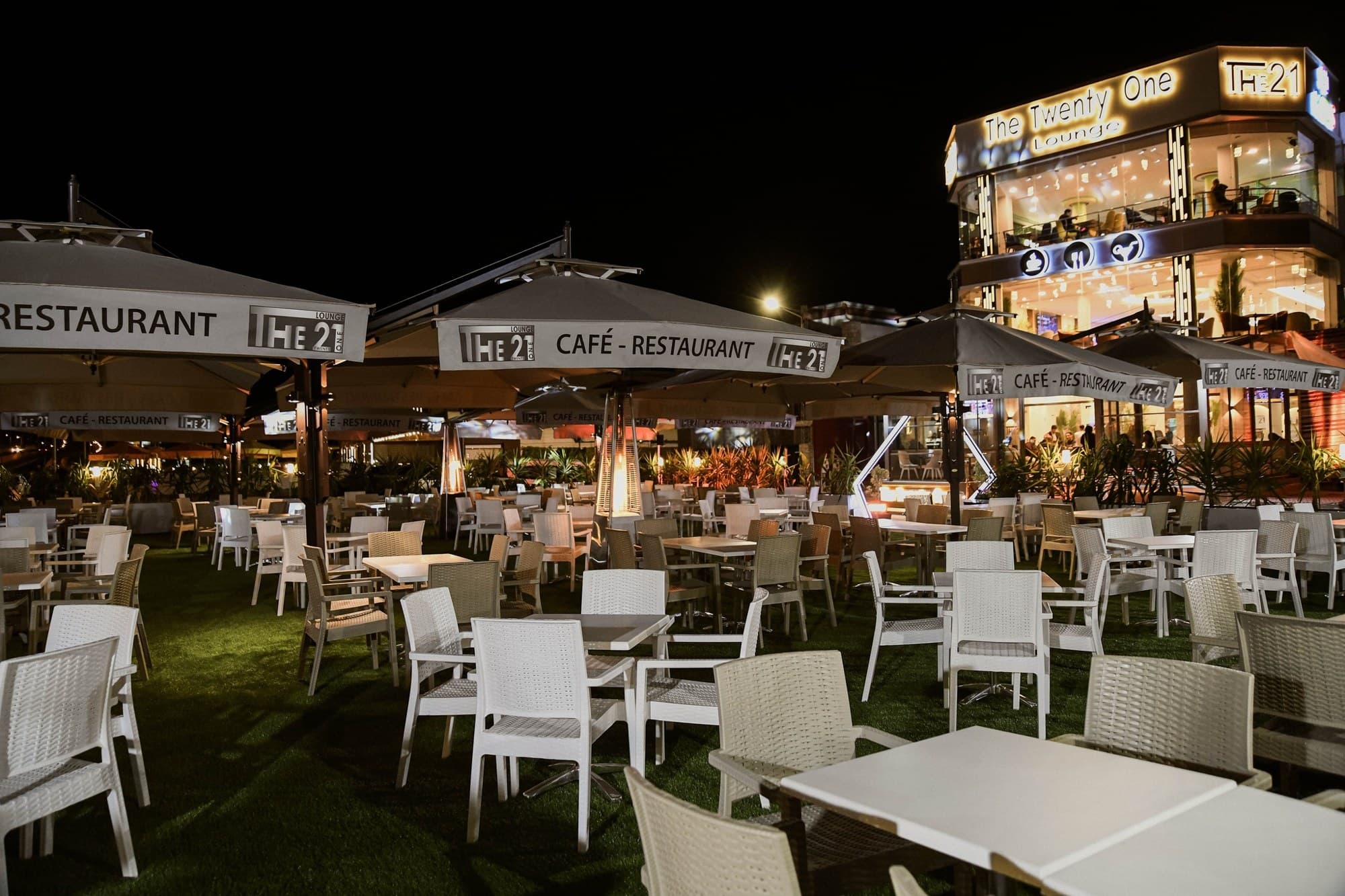 La terrasse du The 21 de nuit, parasols et tables dressées devant la façade illuminée